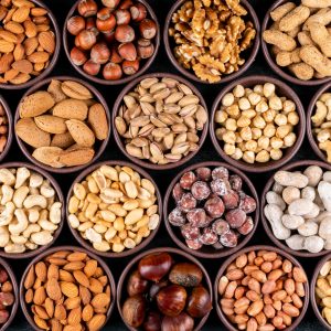 Set of pecan, pistachios, almond, peanut, cashew, pine nuts and lined up assorted nuts and dried fruits in a mini different bowls on a black stone background. flat lay.